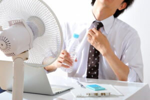 職場での熱中症対策として扇風機と水分補給を実践するビジネスパーソン