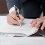 書類を確認しながらペンを持つビジネスパーソンの手元。労務管理や是正指導対応のイメージ