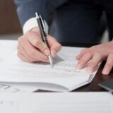 書類を確認しながらペンを持つビジネスパーソンの手元。労務管理や是正指導対応のイメージ