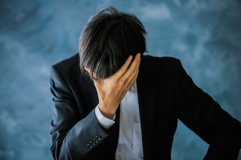 ストレスを抱えて頭を抱えるビジネスパーソン。精神障害の労災認定が過去最多を記録している