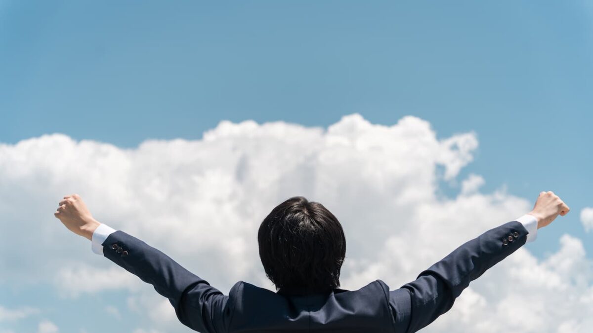 青空と雲を背景に両腕を広げるビジネスマン