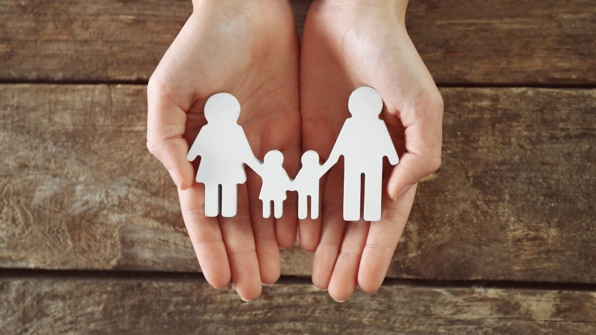 両手で家族の切り絵を包み込む様子。子ども・子育て支援金で社会全体で子育てを支えるイメージ