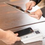 タブレットとスマホ決済端末を操作する手元。賃金のデジタル払い・キャッシュレス決済のイメージ