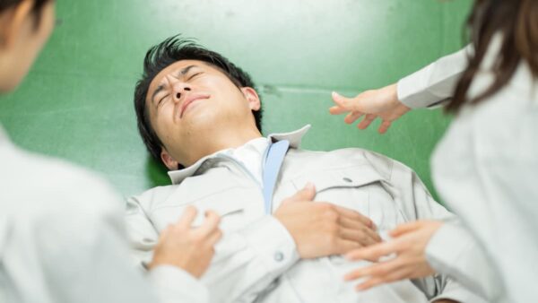 作業服を着た男性が倒れ、同僚が駆け寄る様子。労働災害発生時のイメージ