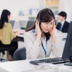 ヘッドセットを付けて顧客対応に苦慮するコールセンターの女性社員