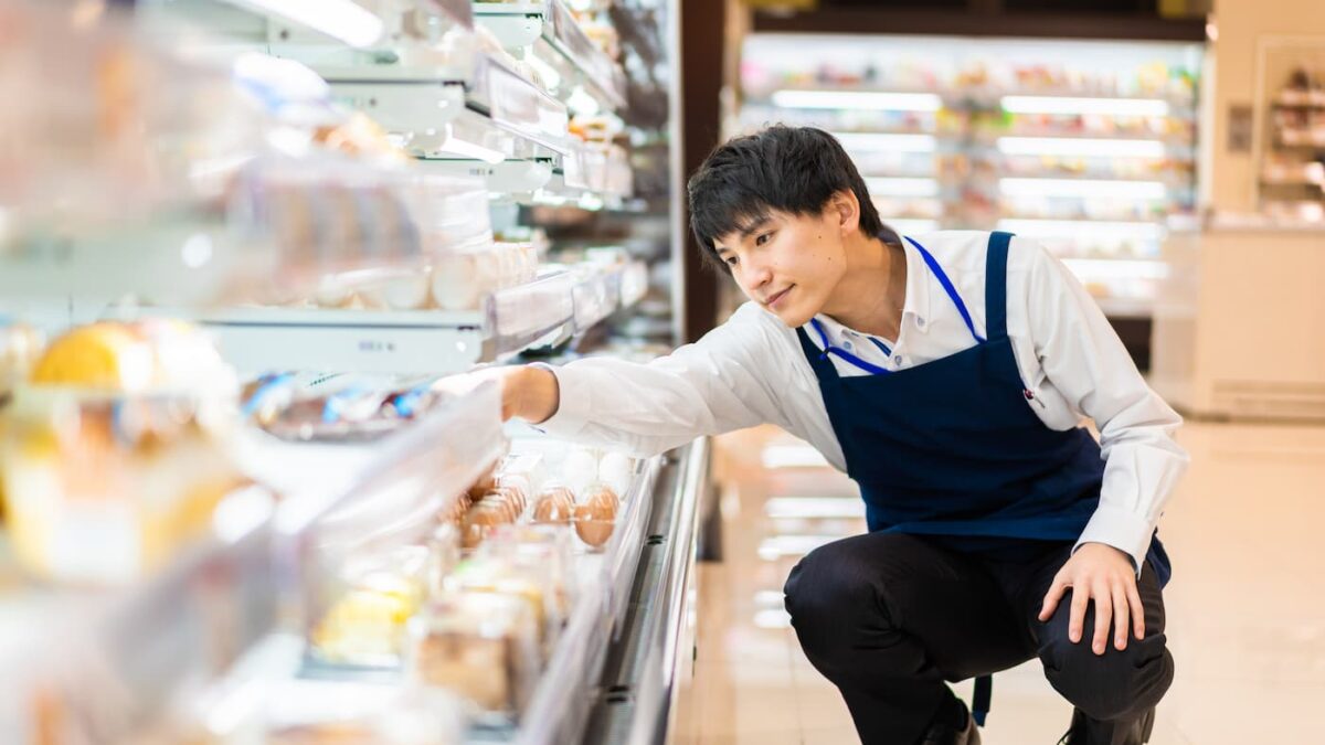 スーパーの冷蔵陳列棚で品出しをするエプロン姿の男性スタッフ