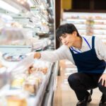 スーパーの冷蔵陳列棚で品出しをするエプロン姿の男性スタッフ